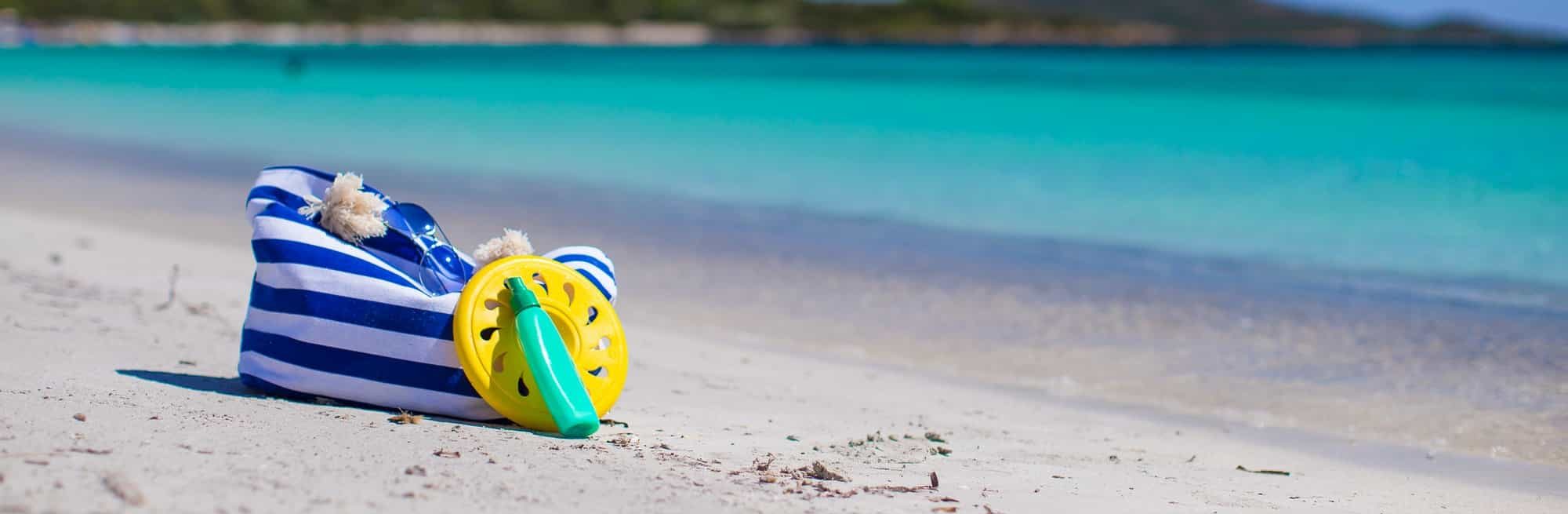 Stripe bag, straw hat, sunblock and frisbee on white sandy tropical beach